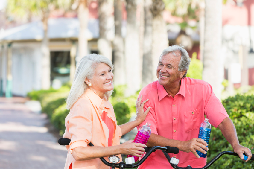 Portrait of a mature couple riding bicycles, taking a break to drink water. They are talking and laughing.
